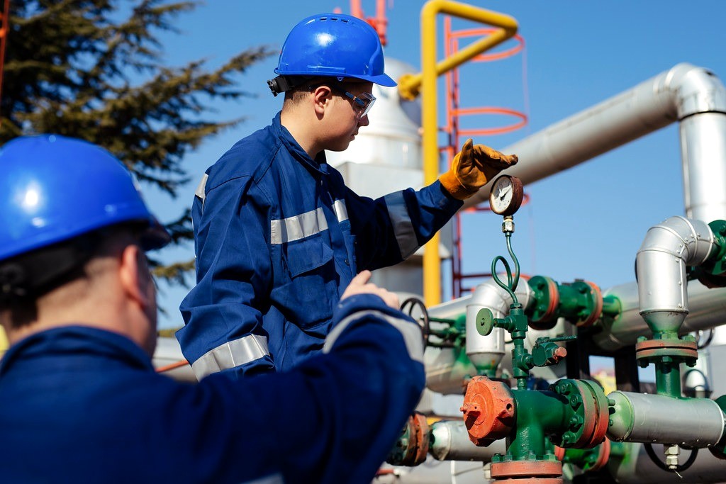 Engineers checking a pressure gauge on refinery pipework